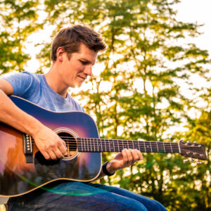 Geronimo playing guitar in front of a sunlit forest